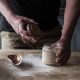 Bubbly sourdough starter in a glass jar on a wooden table. A mans hand is holding on to the lid of the jar. Third build starter