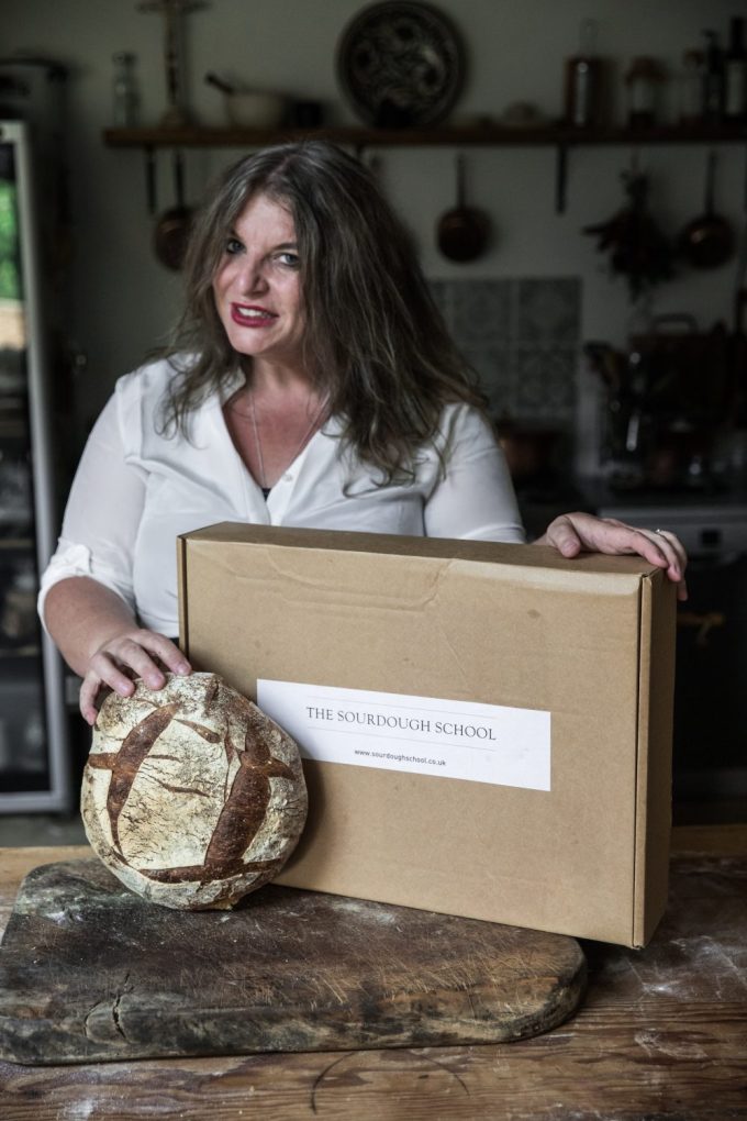 Sourdough expert Vanessa Kimbell holding essentialSourdough baking equipment a the kitchen table with a bread just baked